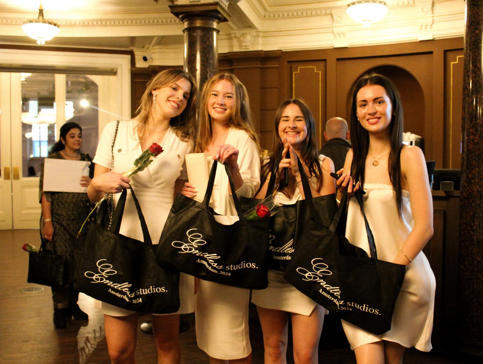 Students at graduation ceremony holding Endless Studios tote bags